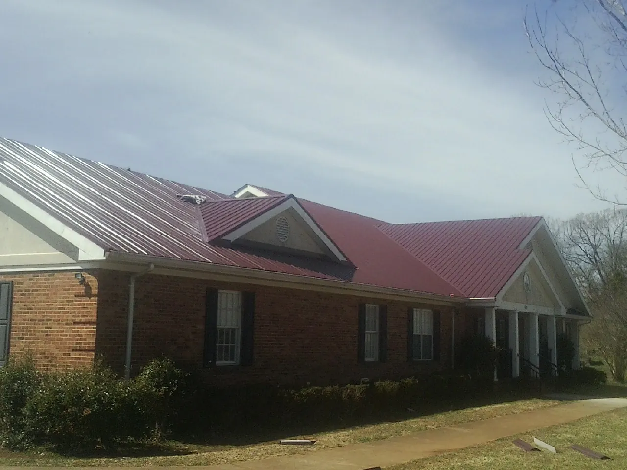 Red metal roof with gabled entries on a long brick building, from a Hail Damage Roof Repair job in Leck Kill