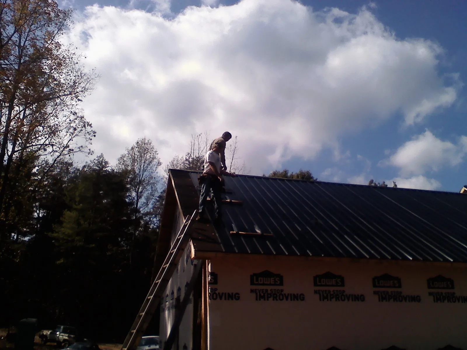 Roofer fastening dark metal panels high against a cloudy sky, from a Roof Inspection job in Leck Kill