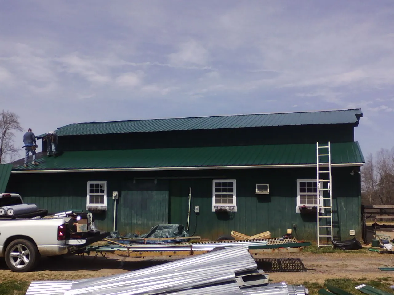 Crew installing green metal roofing on a large green barn in Leck Kill